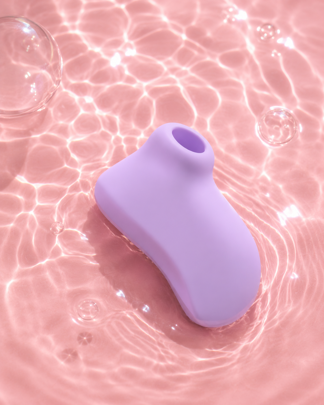 Purple Esmerelda Roco Loco waterproof clitoral suction vibrator resting in shallow pink water with soft light reflections.