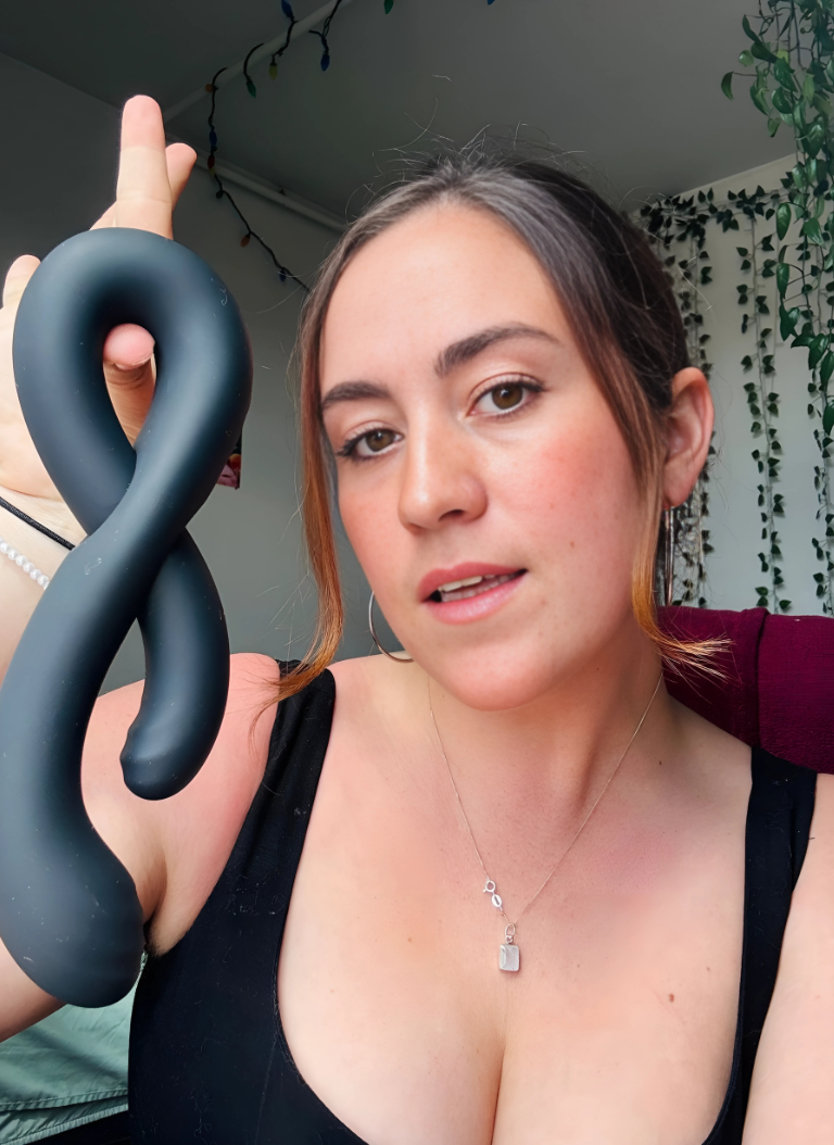 Sex Educator Jill holding the black DuoDiva vibrator, showcasing its unique double-ended design with a confident, inviting expression.