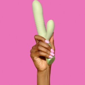 A sleek matcha green dual-stimulation vibrator held confidently in a hand with pink manicured nails against a bold pink background, symbolizing empowerment and pleasure.