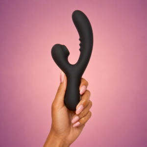 Black SweetSpots dual-stimulation vibrator held against a warm pink background.