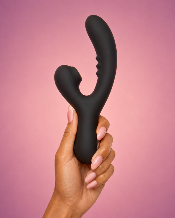 Black SweetSpots dual-stimulation vibrator held against a warm pink background.