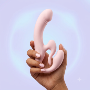 Pale pink Rosé All Day strapless couples vibrator held in a hand against a soft lavender and blue studio background.