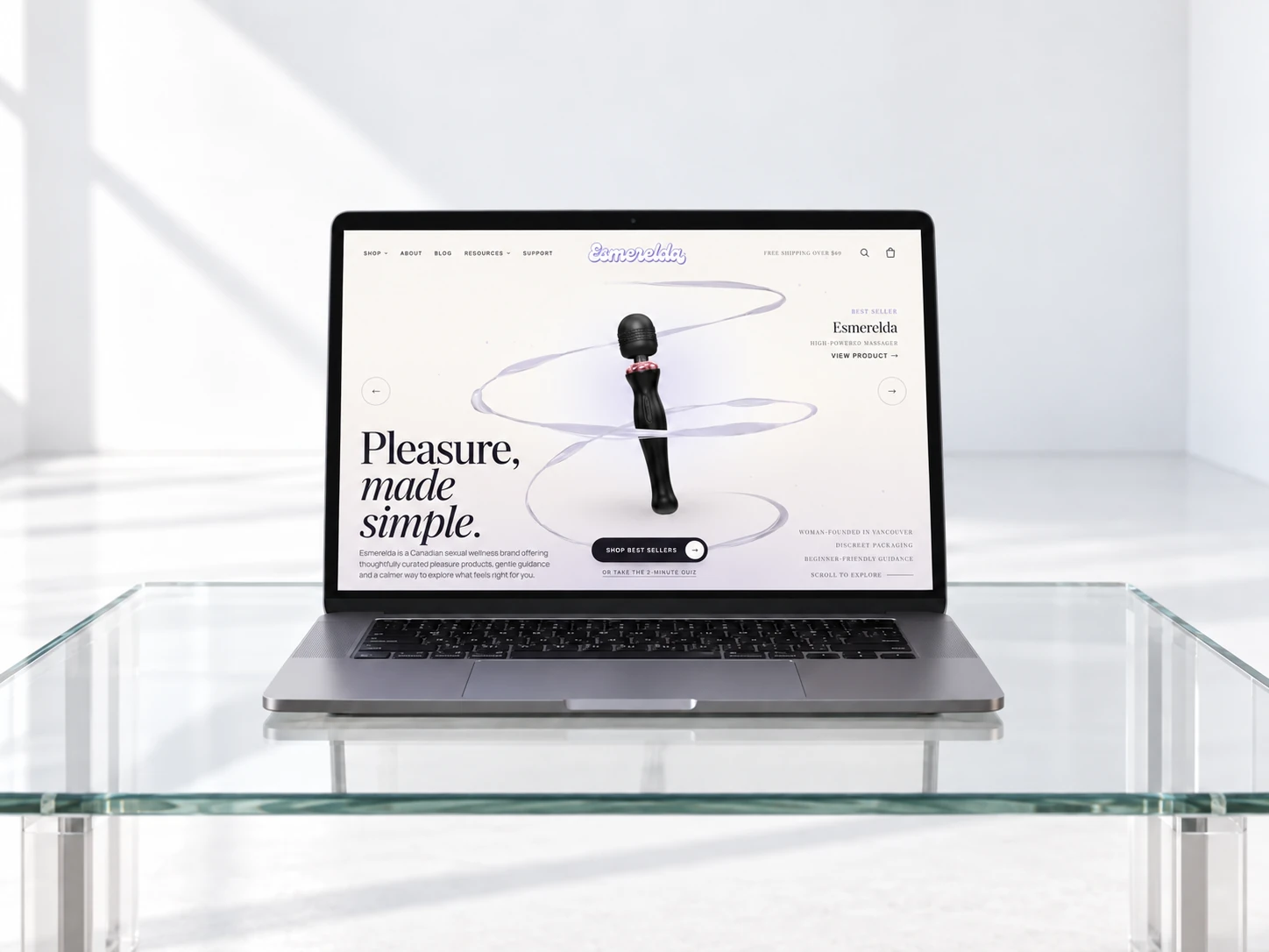 Laptop on a glass table displaying the redesigned Esmerelda homepage, with navigation for Shop, About, Blog, Resources and Support, a "Pleasure, made simple." headline, and a "Shop Best Sellers" call to action.
